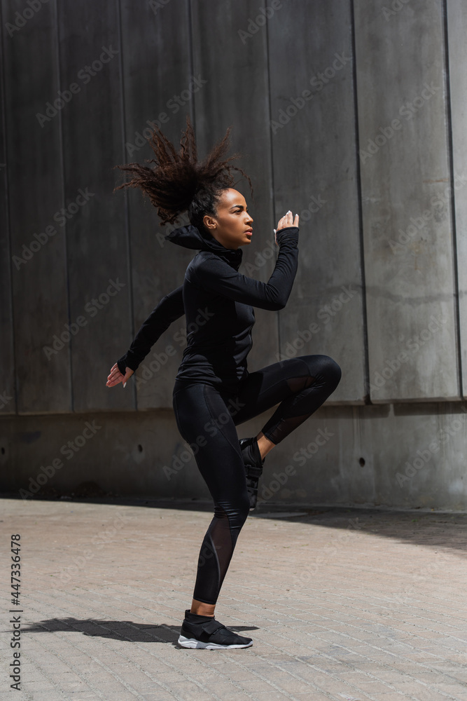 Side view of african american sportswoman warming up on urban street