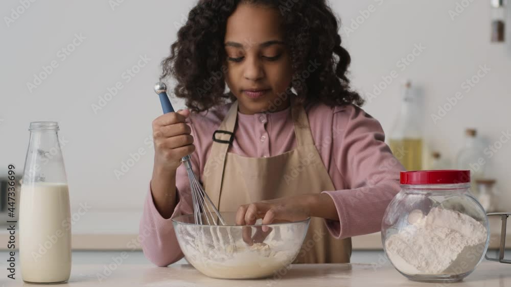 Little african american girl preparing baking at kitchen, trying taste of raw pastry and smiling, enjoying it, slow motion Little african american girl preparing baking at kitchen, trying taste of raw pastry and smiling, enjoying it, slow motion