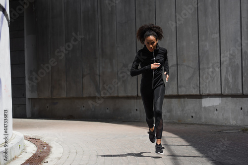 Young african american woman looking at camera while jogging on urban street