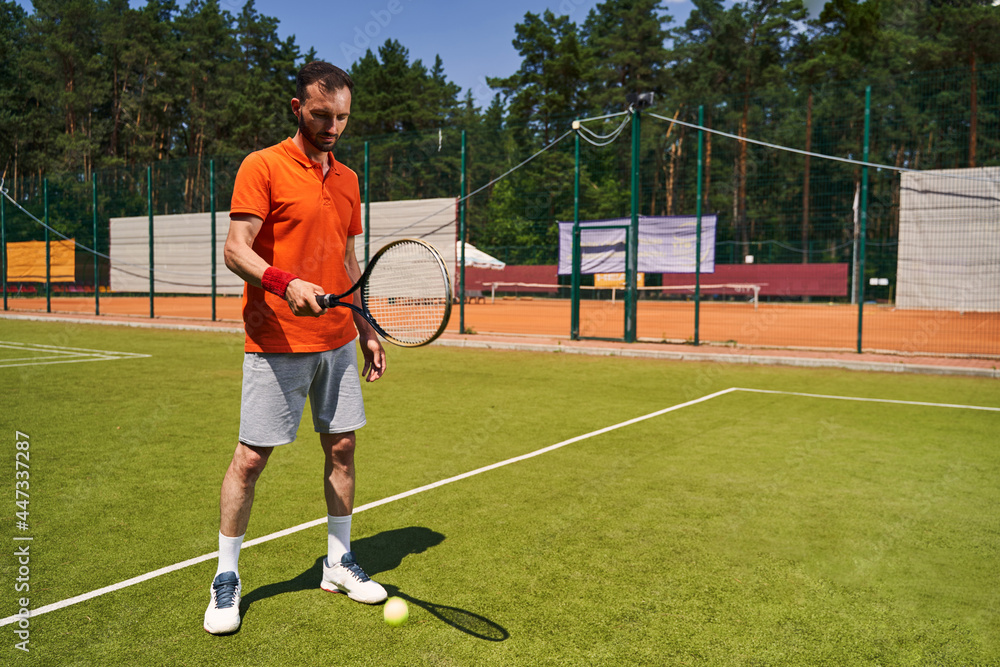Dark-haired bearded mustached professional tennis player training on the court