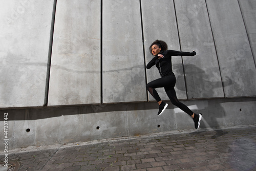 African american sportswoman running near concrete wall