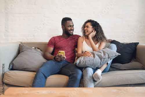 Couple using a mobile phone while sitting on a couch at home.