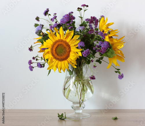 sunflowers and purple ageratum in a glass vase .