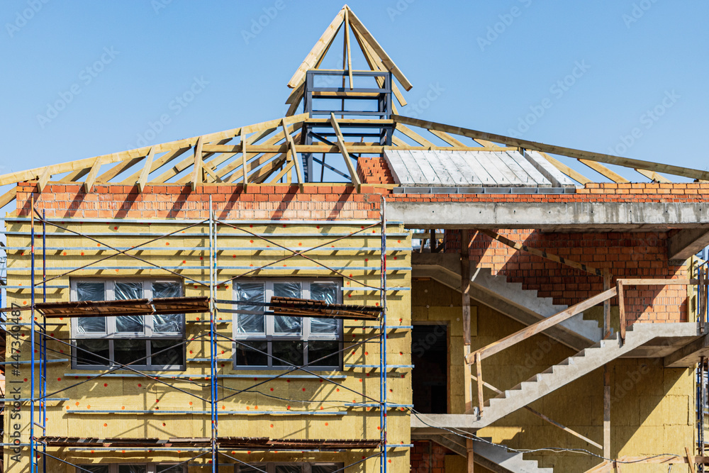 Thermal insulation of a red brick house with mineral wool. The use of scaffolding when building a house.