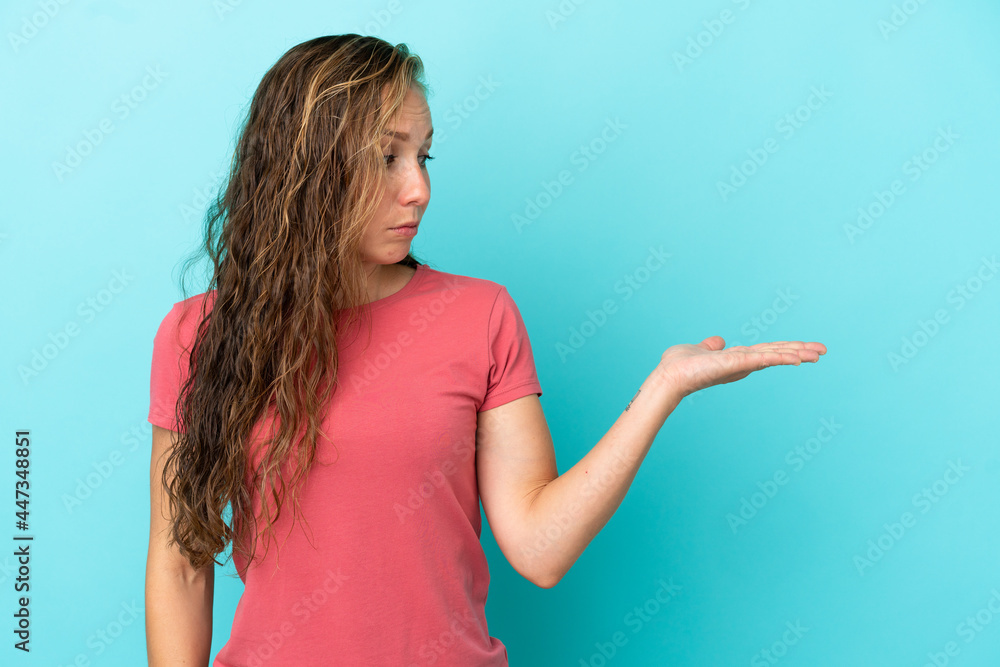 Young caucasian woman isolated on blue background holding copyspace with doubts Young caucasian woman isolated on blue background holding copyspace with doubts