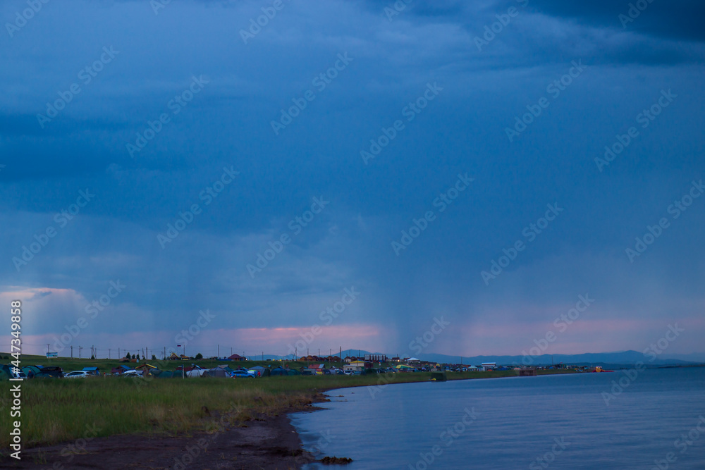 Tent camp on the shore of the lake. Camping summer vacation by the water. Landscape at sunset during the rain