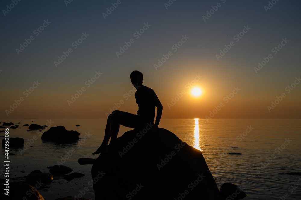 European man depressing and sitting on a large rock in the sea at sunset.