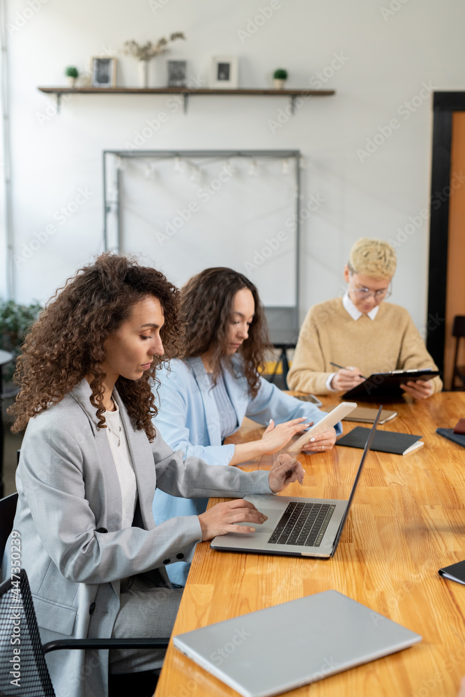 Three contemporary female managers working individually by table in boardroom Three contemporary female managers working individually by table in boardroom
