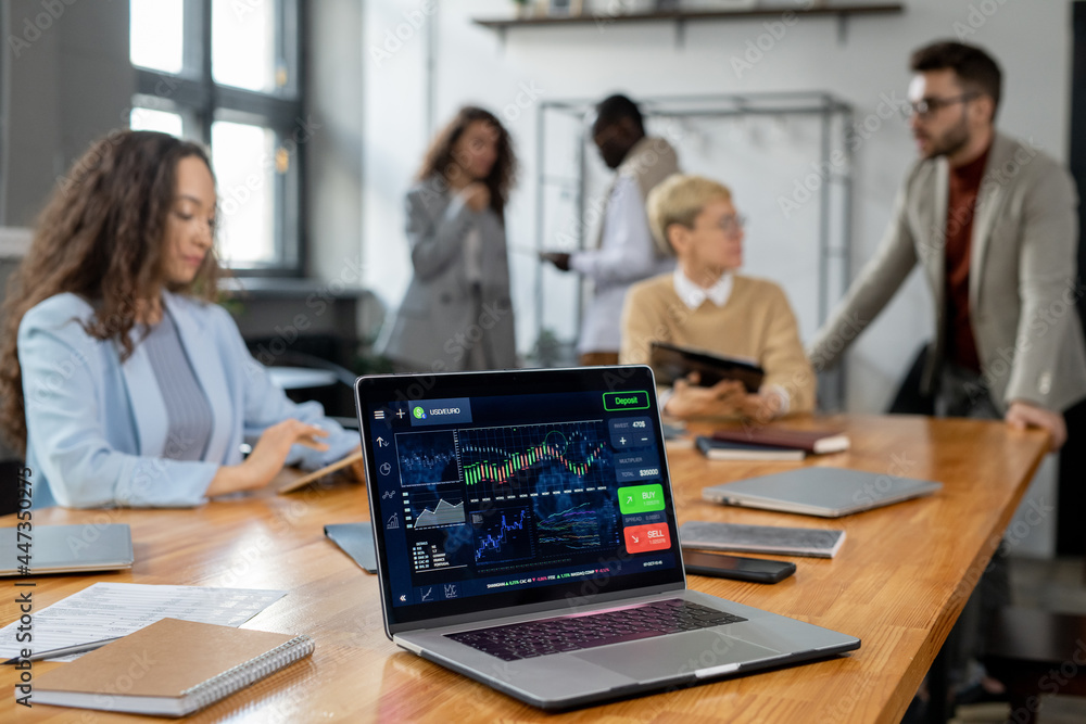 Laptop display with financial graph and other data on workplace where group of managers co-working Laptop display with financial graph and other data on workplace where group of managers co-working
