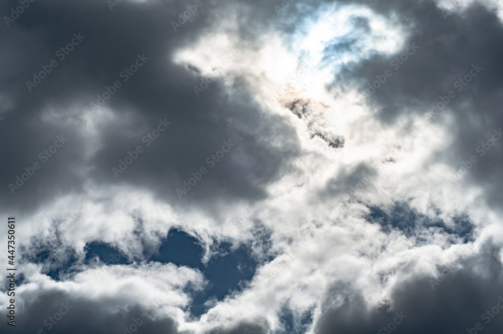 White-gray cloudy clouds against dark blue sky, sun came out from behind clouds. White-gray cloudy clouds against dark blue sky, sun came out from behind clouds.