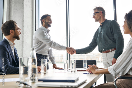 Obraz na płótnie Two happy diverse professional business men executive leaders shaking hands after successful financial deal at group board office meeting