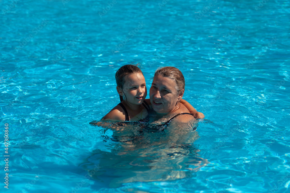 Grandmother and granddaughter in pool. A beautiful grandmother and a sweet granddaughter are embracing in the clear water of the pool, love and respect in the family have passed through generations. Grandmother and granddaughter in pool. A beautiful grandmother and a sweet granddaughter are embracing in the clear water of the pool, love and respect in the family have passed through generations.
