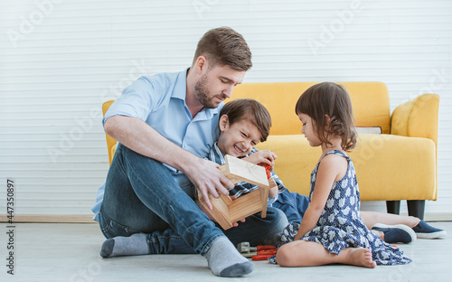 Handsome Caucasian father and little cute son, sweet daughter playing toys together with happiness and fun in cozy living room at home on weekend holidays. Family and Education Concept.