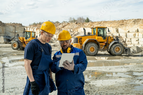 Two builders in workwear looking at sketch of building on tablet screen photo