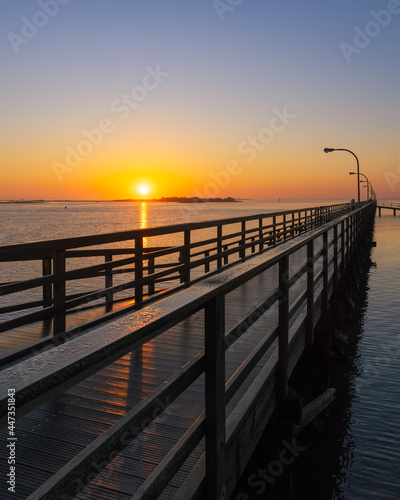 Sun on the horizon illuminating a wooden boardwalk fishing pier with golden light. Captree State Park  New York