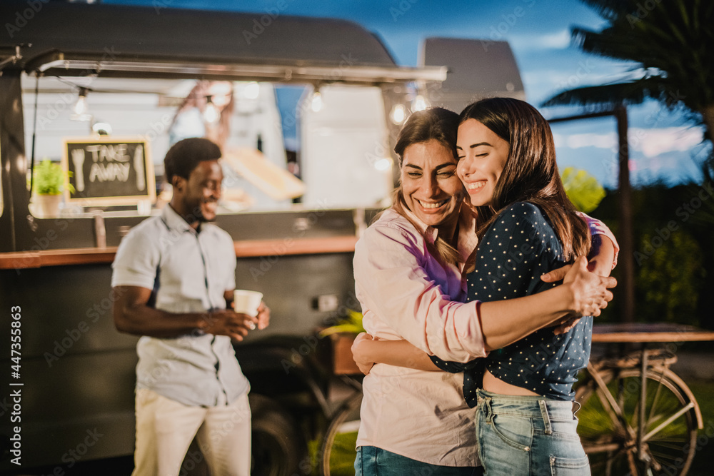 Cheerful girlfriends hugging near food truck