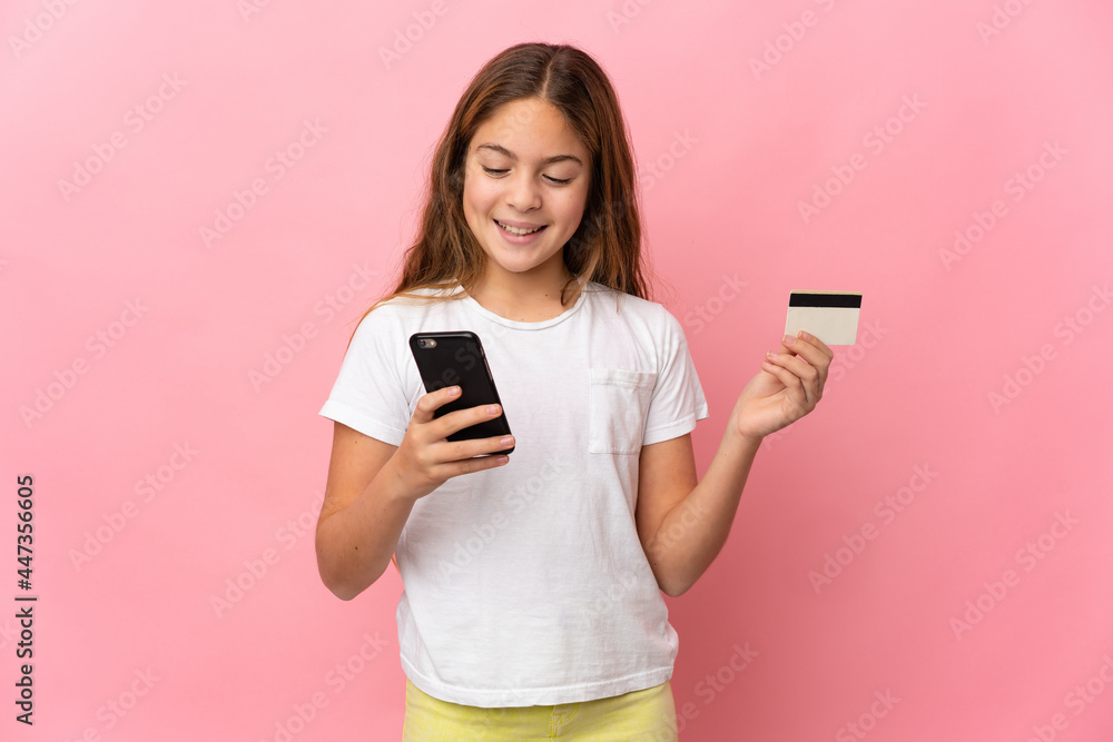 Child over isolated pink background buying with the mobile with a credit card Child over isolated pink background buying with the mobile with a credit card