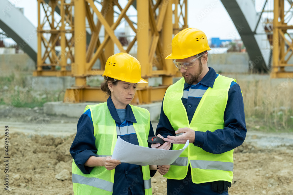 Two engineers working in team they standing on the site and discussing blueprint of future building Two engineers working in team they standing on the site and discussing blueprint of future building