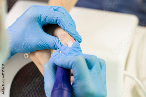 A manicure master in a mask and gloves does a manicure  removes the cuticle to the client from above