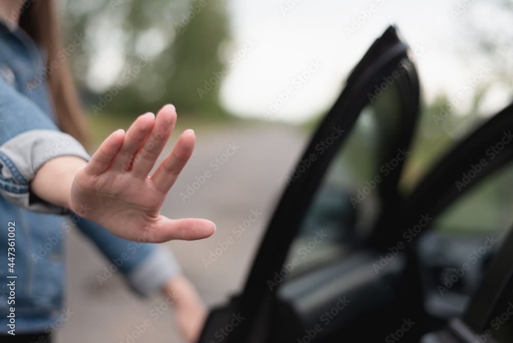 Woman shows a stop gesture by her palm and walks away from a car.