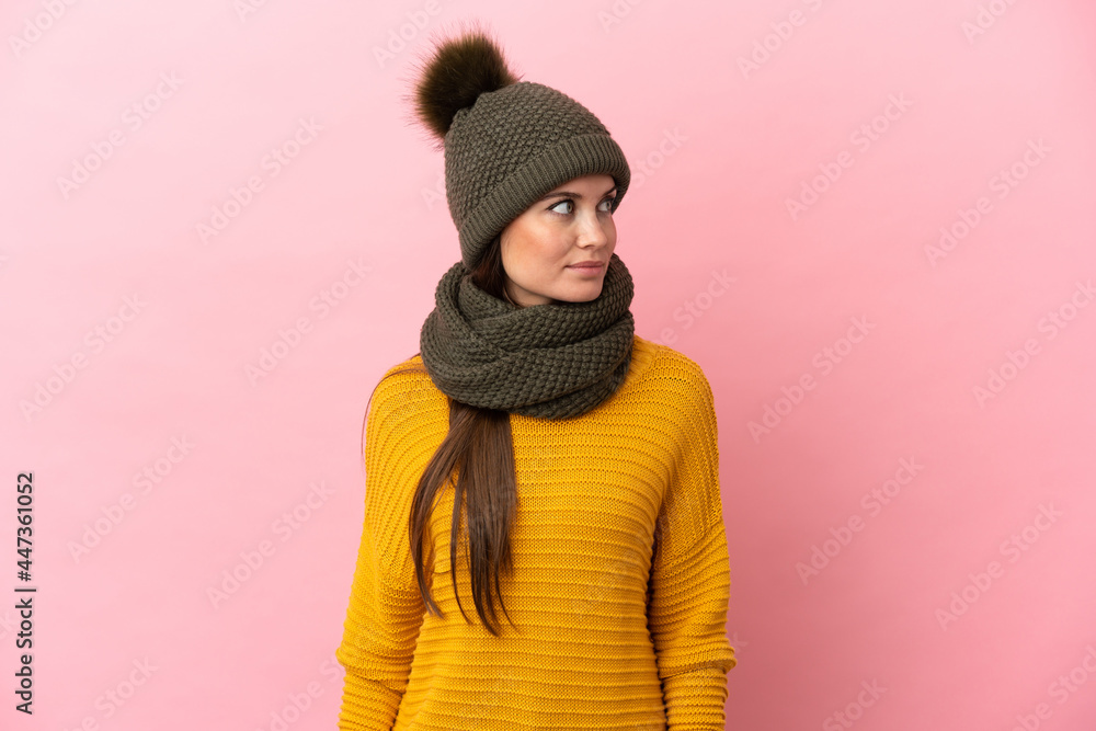 Young caucasian girl with winter hat isolated on pink background looking to the side Young caucasian girl with winter hat isolated on pink background looking to the side