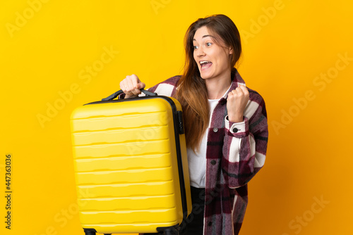 Young Ireland woman isolated on yellow background in vacation with travel suitcase