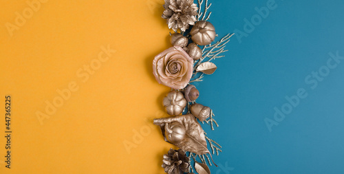 Flat lay of golden acorns, cones, leaves and pumpkins on an orange-turquoise background. Minimalistic autumn concept with copy space. Banner format © Alina