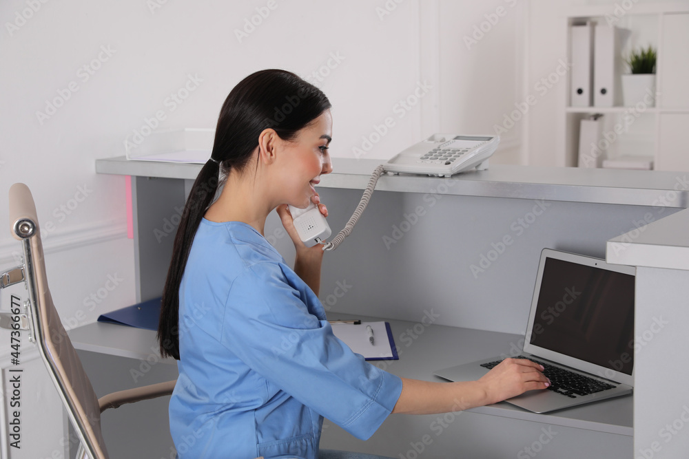 Receptionist talking on phone at workplace in hospital