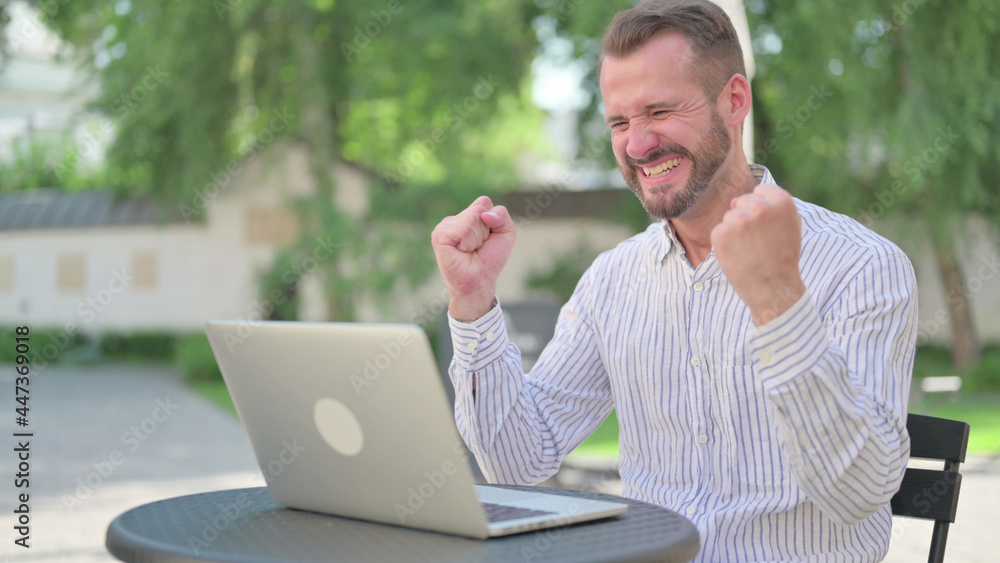 Successful Mature Adult Man Celebrating on Laptop in Outdoor Cafe Successful Mature Adult Man Celebrating on Laptop in Outdoor Cafe