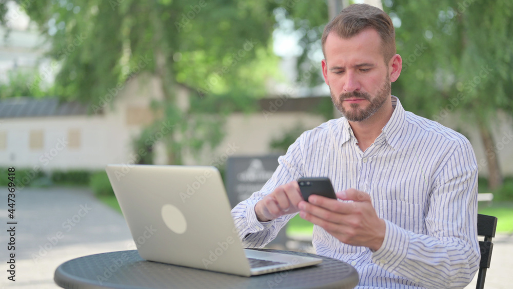 Mature Adult Man Browsing Internet on Smartphone in Outdoor Cafe Mature Adult Man Browsing Internet on Smartphone in Outdoor Cafe