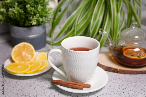 A hot tea drink with lemon and orange, a teapot and a white cup, served with delicious lemon and cinnamon. Fragrant and warming tea