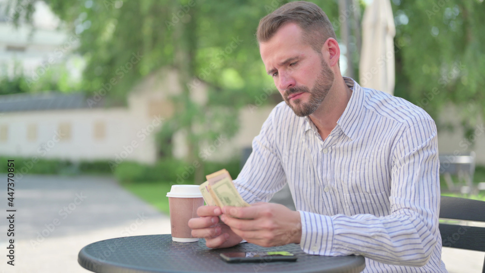 Mature Adult Man Counting Dollars while Sitting in Outdoor Cafe Mature Adult Man Counting Dollars while Sitting in Outdoor Cafe