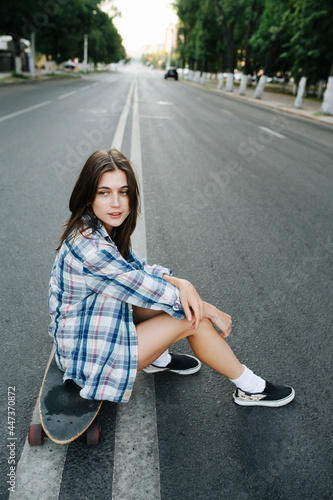 Pretty woman sitting on a skateboard in the middle of an empty city road © zzzdim