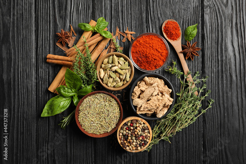 Different natural spices and herbs on black wooden table, flat lay