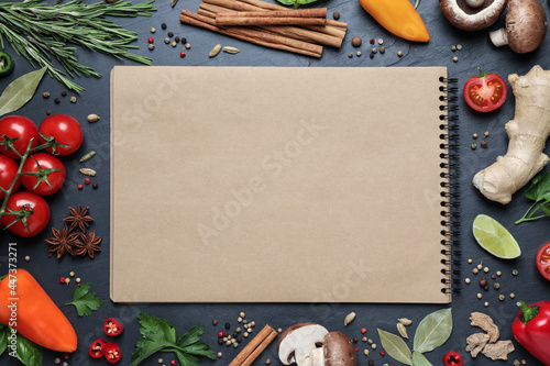 Open recipe book and different ingredients on black table, flat lay. Space for text photo