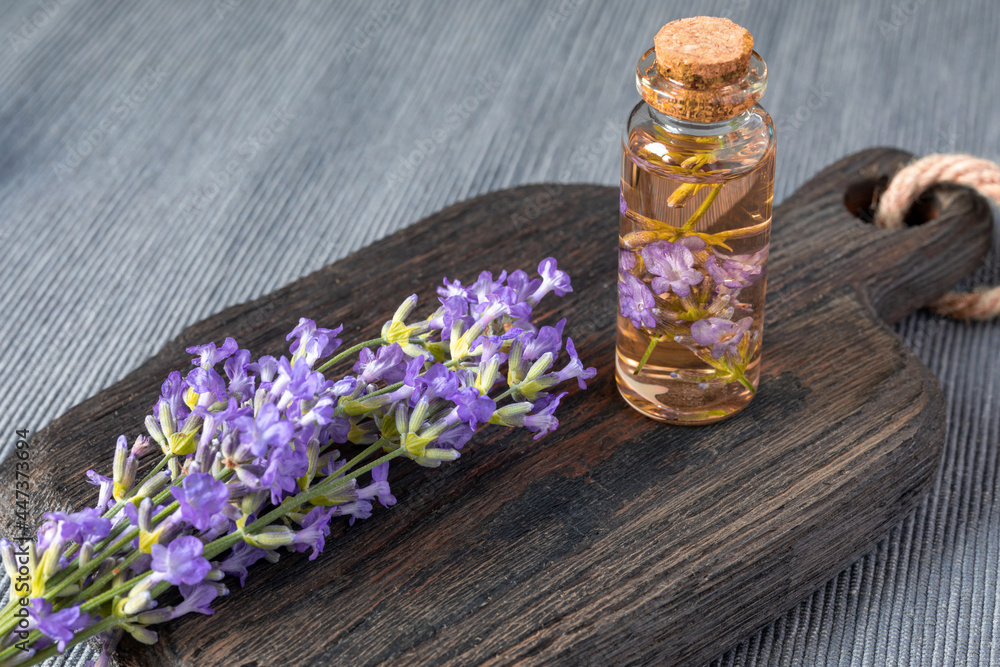 Bunch of blooming lavender and small glass bottle with essential lavender oil and flowers on wooden kitchen board. Traditional medicine, cosmetology or aromatherapy concept Bunch of blooming lavender and small glass bottle with essential lavender oil and flowers on wooden kitchen board. Traditional medicine, cosmetology or aromatherapy concept