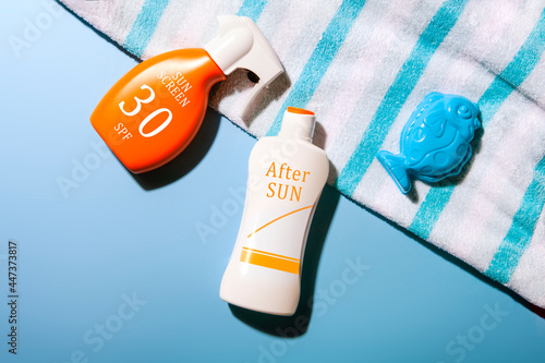 top view of Sun screen and after sun lotion set on blue background with a fish mold and a striped towel. summer care concept.