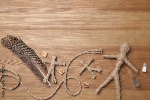 Voodoo doll pierced with pins and ceremonial items on wooden table, flat lay. Space for text