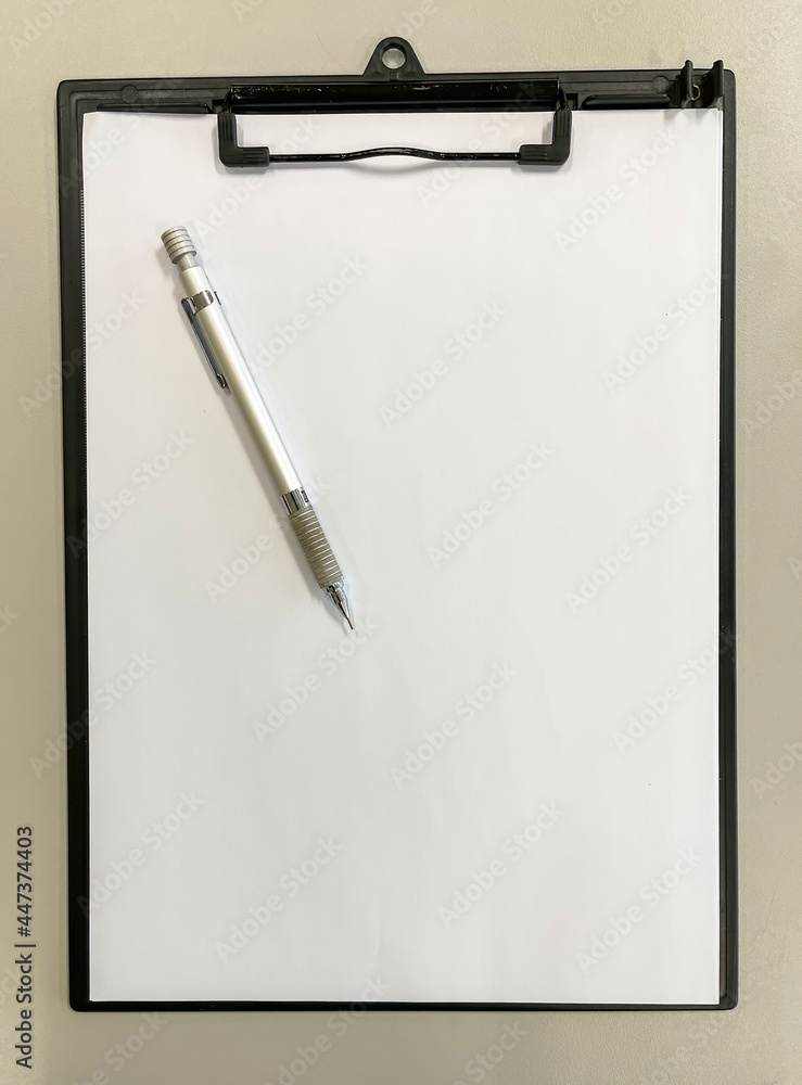 top view of a black clipboard folder with a blank sheet of paper and a metal mechanical pencil on a grey table, copy space, vertical