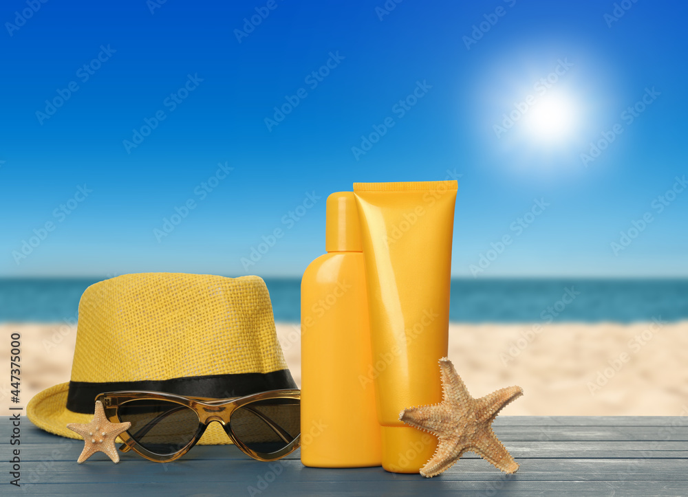 Skin sun protection products and beach accessories on blue wooden table against seascape. Space for design
