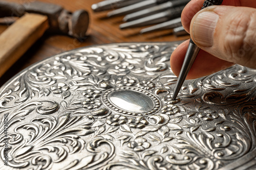 Photos CLOSEUP OF CRAFTSMAN'S HAND EMBOSSING SILVER OR METAL WITH PUNCH IN THE WORKSHOP