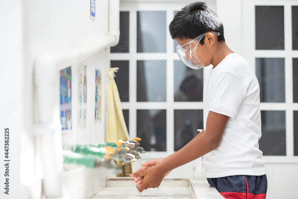 Mexican student washing hands at school and wearing plastic face mask Mexican student washing hands at school and wearing plastic face mask