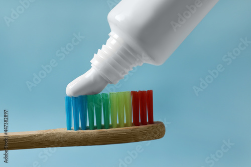 Squeezing toothpaste onto brush against light blue background  closeup