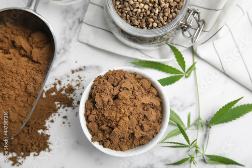 Hemp protein powder, seeds and fresh leaves on white marble table, flat lay