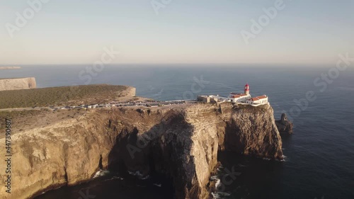 Cinematic aerial shot of Cape Saint Vincent lighthouse on eroded high cliff surrounded by Atlantic Ocean.