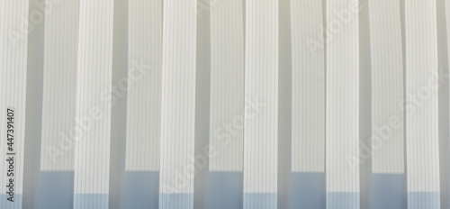 Abstract geometric vertical lines white and gray gradient color. Repeating pattern, background texture, design of striped lines. Blinds illuminated by the sun, close-up. © exebiche