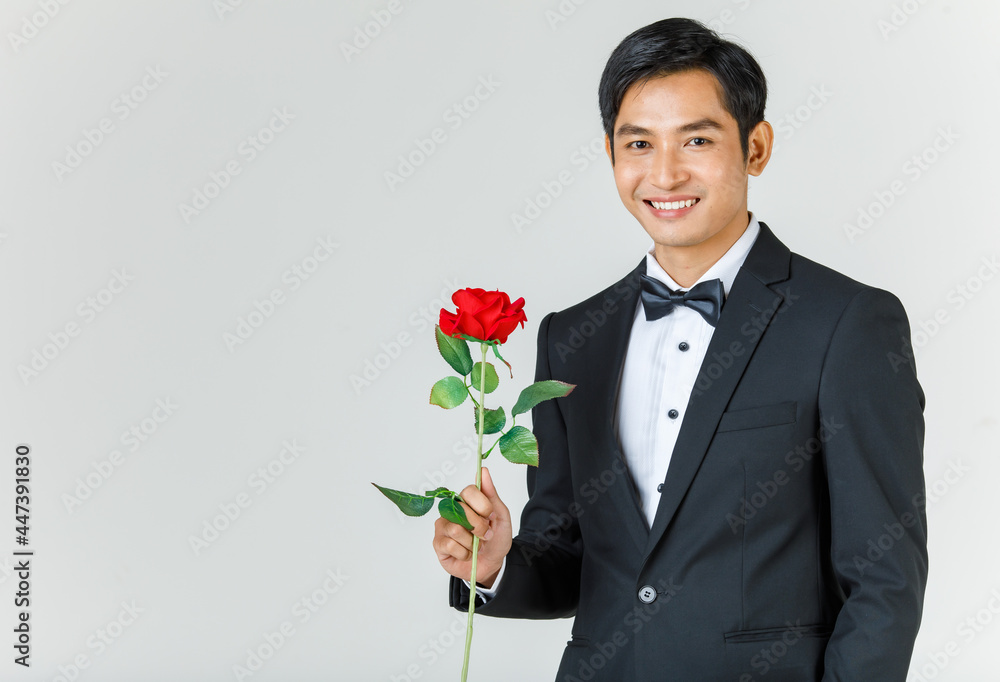 Young attractive Asian man, soon to be groom wearing black tuxedo smiling and holding rose. Concept for pre wedding photography Young attractive Asian man, soon to be groom wearing black tuxedo smiling and holding rose. Concept for pre wedding photography