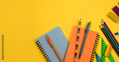 Stationery is on a yellow background. Top view of notepads, pens and colored pencils on a yellow background. Education concept.
