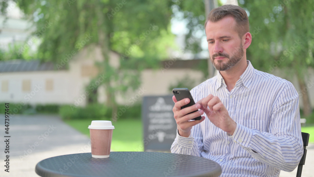 Mature Adult Man Browsing Internet on Smartphone in Outdoor Cafe Mature Adult Man Browsing Internet on Smartphone in Outdoor Cafe