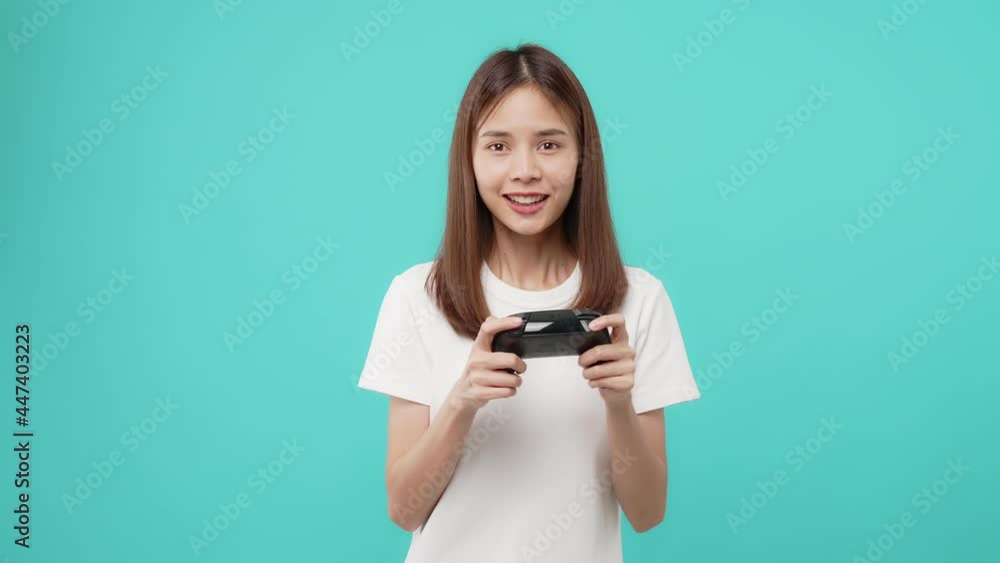 Excited young Asian woman playing games on joystick on blue background. Excited young Asian woman playing games on joystick on blue background.